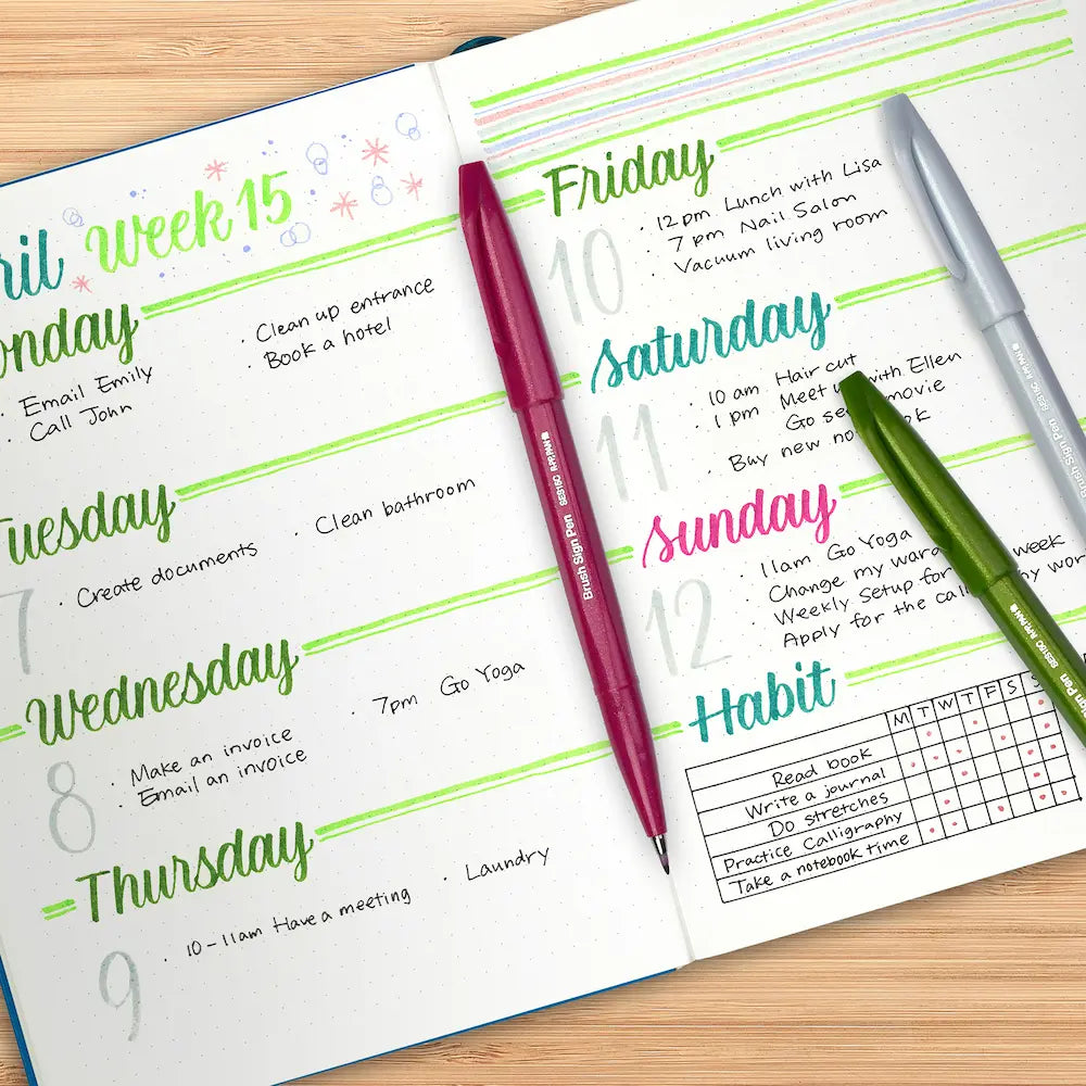 Weekly planner with handwritten tasks written with Pentel Brush Sign Pens and the three pens on a wooden table.